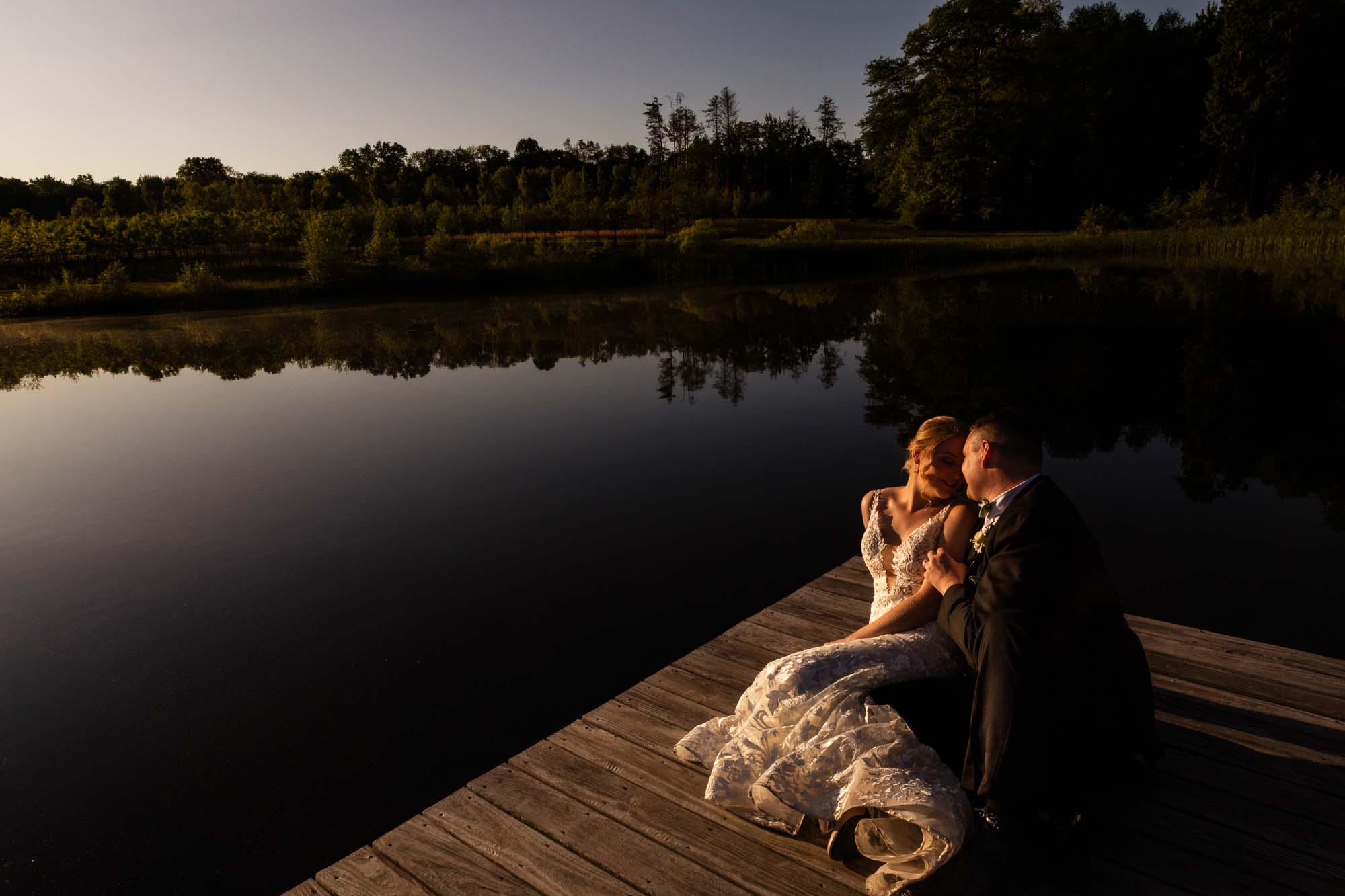 bride and groom snuggling together on the dock at sunset, surrounded by a beautiful lake at the pinehall at eisler farms wedding venue